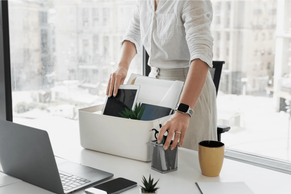 Une femme est à son bureau et rassemble ses effets personnels dans une boite.